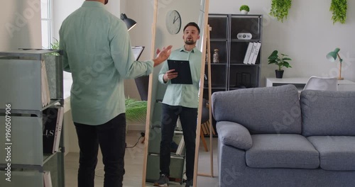 Man holds a clipboard, preparing for rehearsal and presentation, checking reflection in a mirror. Man rehearses presentation in front of mirror. Employee prepare for job conference at home
