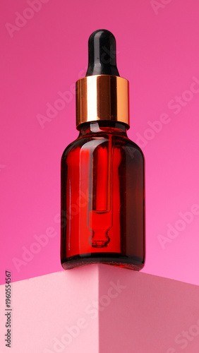 Bottle of serum on a pink background with a simple display setup
