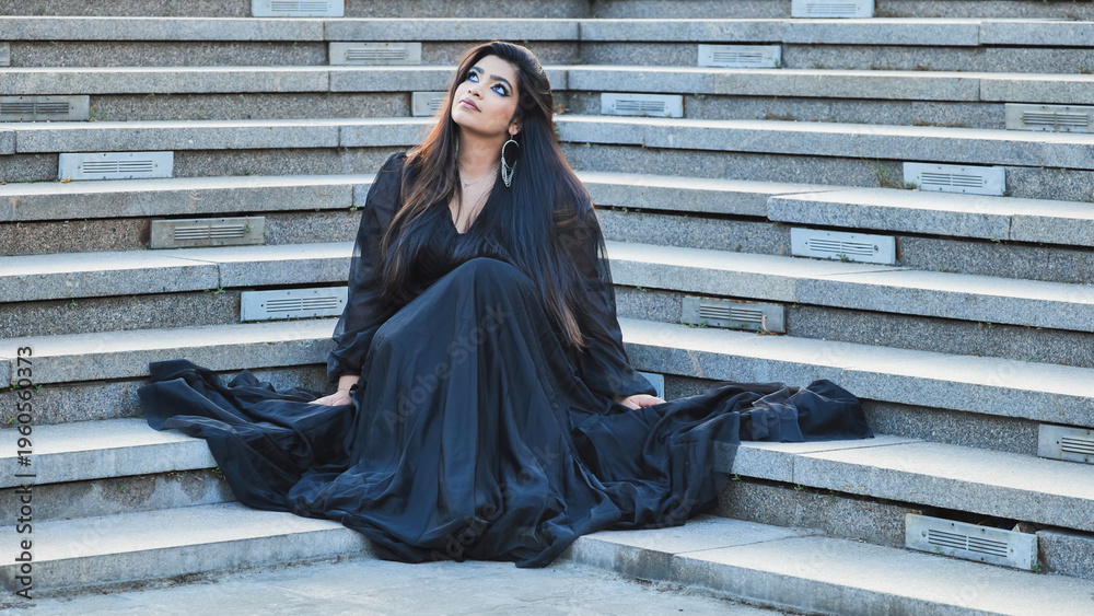 Naklejka premium Bangladeshi woman sitting on stairs in black dress, looking up, dreaming of future
