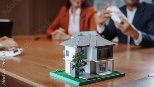 Happy couple signing documents with agent, receiving key, model house on table, real estate purchase or mortgage approval in modern office.