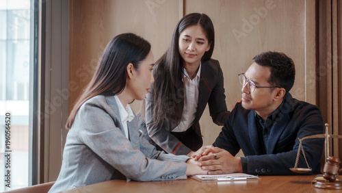 Foto Lawyer or mediator meeting with clients, hands joined in support at desk with contract, judge gavel and scales of justice in foreground, professional office setting