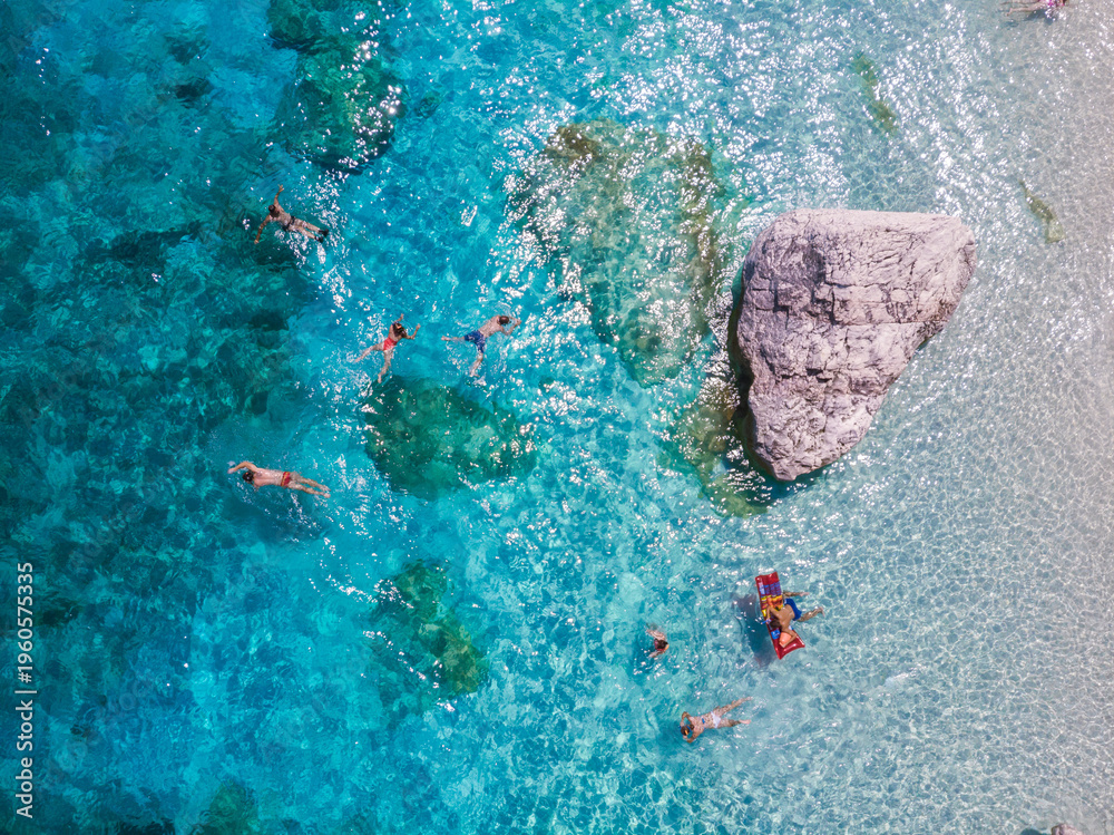 Obraz premium People enjoy a blissful day swimming and relaxing in the crystal-clear waters of Sardinia, captivated by the stunning natural beauty of Baunei. The sun shines brightly over the vibrant landscape.