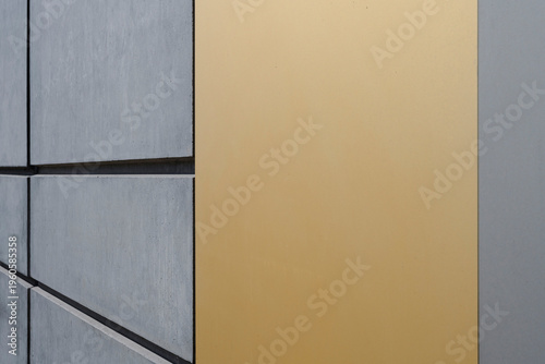 Abstract close-up of a building facade with gray concrete panels and a contrasting golden yellow section. Clean lines and geometric architectural design