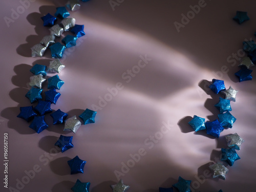 Top view of blue paper stars on a pastel backdrop featuring artistic light play. High-quality aesthetic background for greeting cards, social media posts, and modern stationary branding.