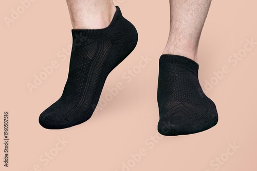 A pair of black low-cut athletic socks on male feet against a peach background provides a clean, minimalist product showcase.