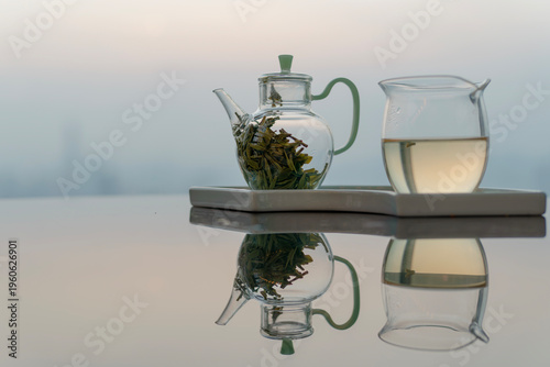 Glass teapot and fair cup on reflective table with city skyline