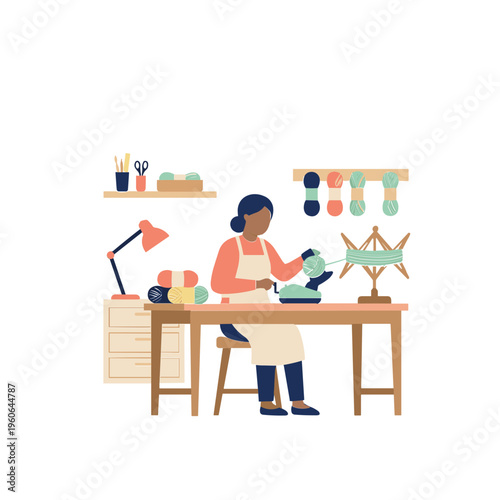A woman sews on an ironing board in her workshop surrounded by threads.