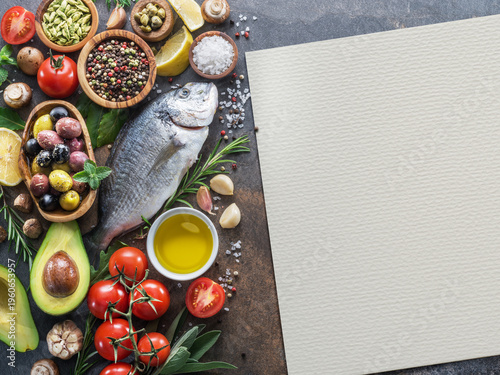 Mediterranean ingredients including fish, olive oil and vegetables arranged on a stone kitchen surface with blank watercolor paper for text or recipe notes.