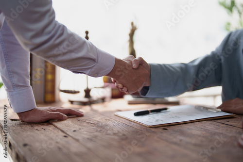 Konstfotografi Two business professionals in formal attire shaking hands over a wooden desk wit