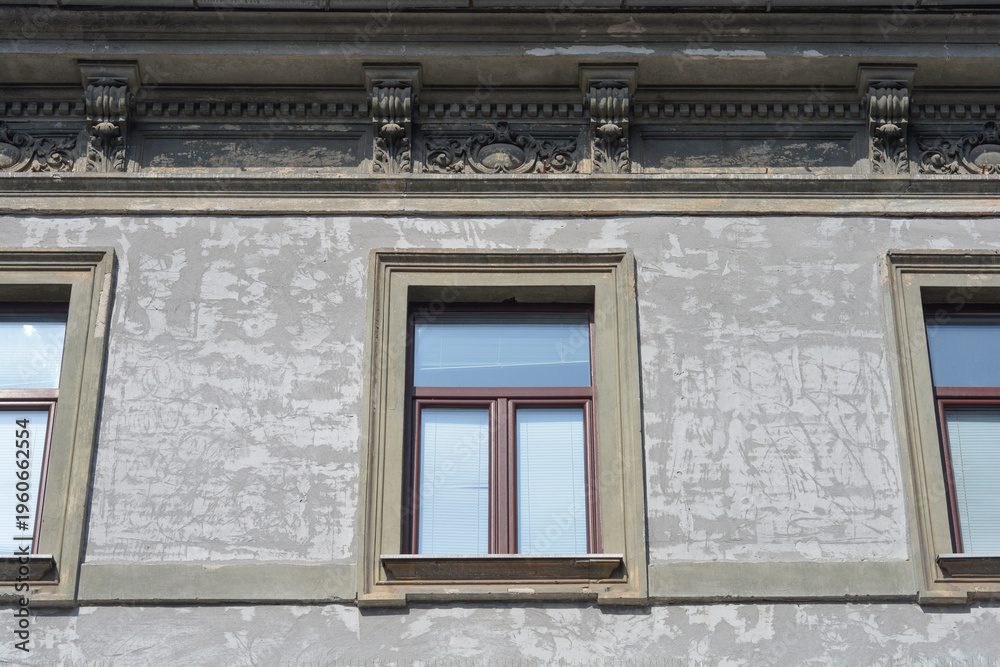 Obraz premium Three brown wooden windows are set into a rough weathered grey building facade featuring decorative stone consoles on the upper cornice