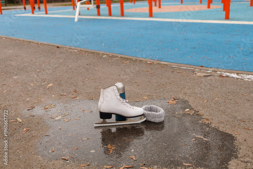 A white ice skate rests on a wet surface beside a playground with bright colors