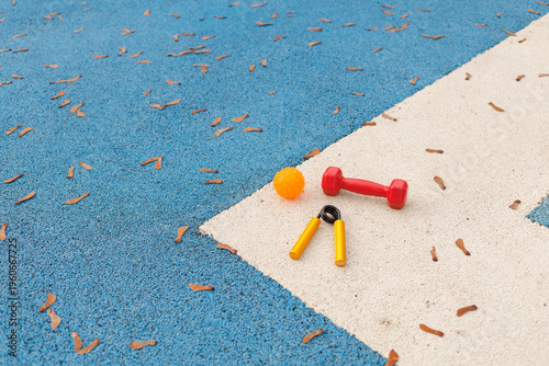Small weights, a ball, and a pair of scissors are on a blue sports court covered with leaves