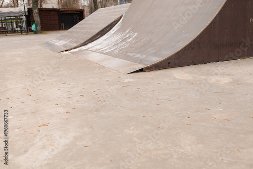 Two metal ramps are set up in a park with trees around and a wooden structure in the background
