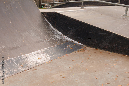 A skateboard ramp shows signs of use with a worn surface and scattered leaves around it