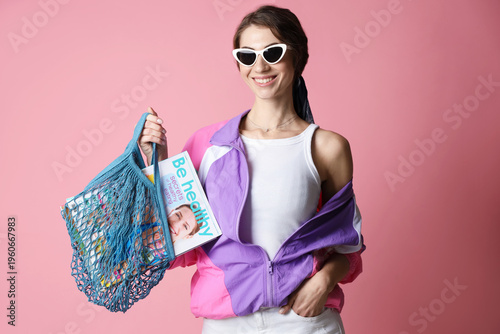 Woman holding net bag with magazines on pink background