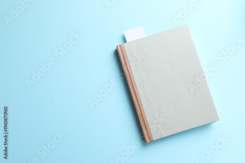 Book with white bookmark on light blue background, top view. Space for text