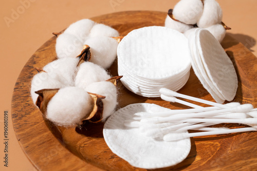 Cotton pads and cotton swabs, delicate cotton flowers on wooden plate, close-up. Concept of eco-friendly makeup removers, facial skin care. Beauty, health, and personal hygiene