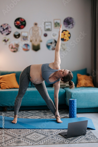 Pregnant woman practicing yoga in living room with online class