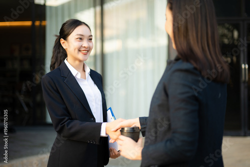 Cuadro en lienzo Two smiling Asian businesswomen in suits shaking hands while standing outside of