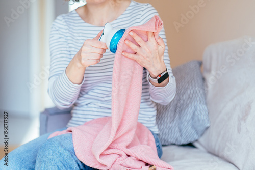 Close up woman hand cleaning pink knitwear with electric fabric shaver