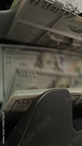 Close-up of a currency counter machine processing one hundred US dollar bills with a focus on Benjamin Franklin's portrait. High-speed money counting concept for banking and finance.