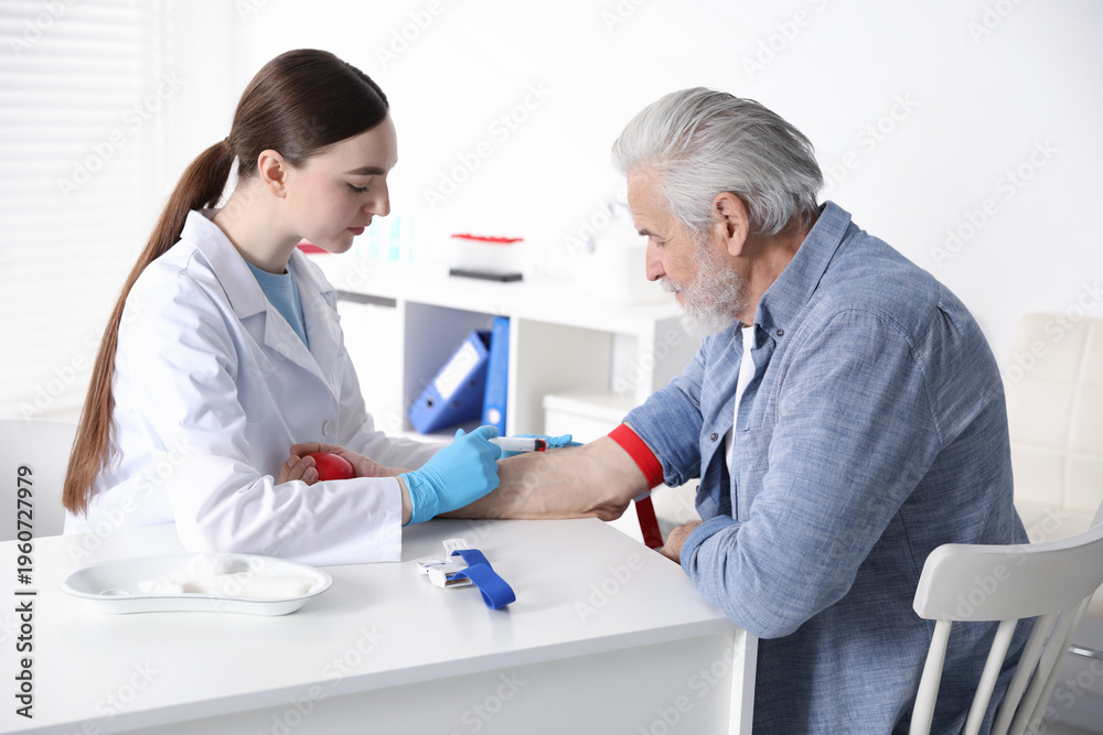 Fototapeta premium Doctor drawing senior man's blood sample in clinic