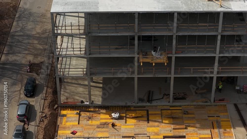 Drone footage capturing a partially completed multi story concrete building with scaffolding, formwork, and materials, highlighting structural progress and active construction environment.