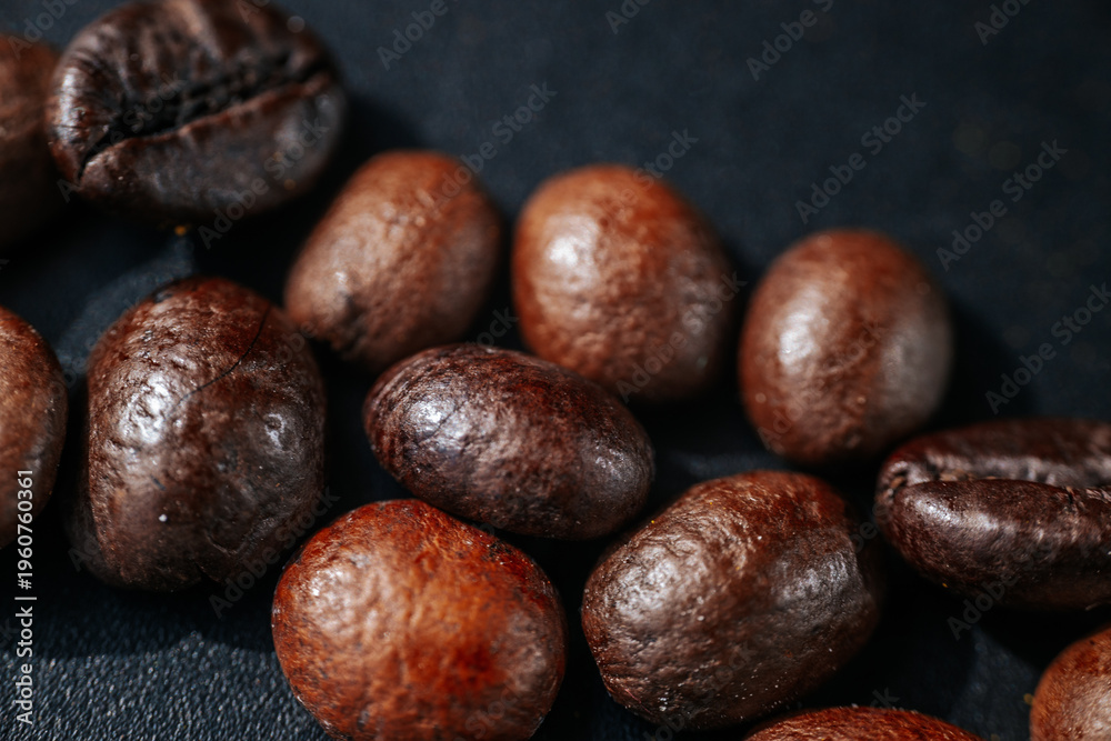 Obraz premium Macro close-up of roasted coffee beans scattered on a dark textured surface, highlighting rich brown tones, an oily sheen, and detailed textures with a shallow depth of field.