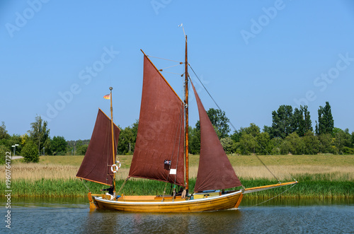 Traditional Zeesboat with brown sails sailing along the embankment of the Zingster Bodden (lagoon), Germany
