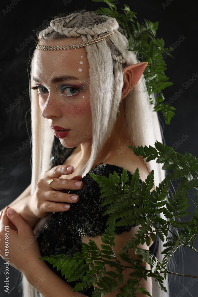Fototapeta premium Beautiful elf girl with floral decor on black background with smoke