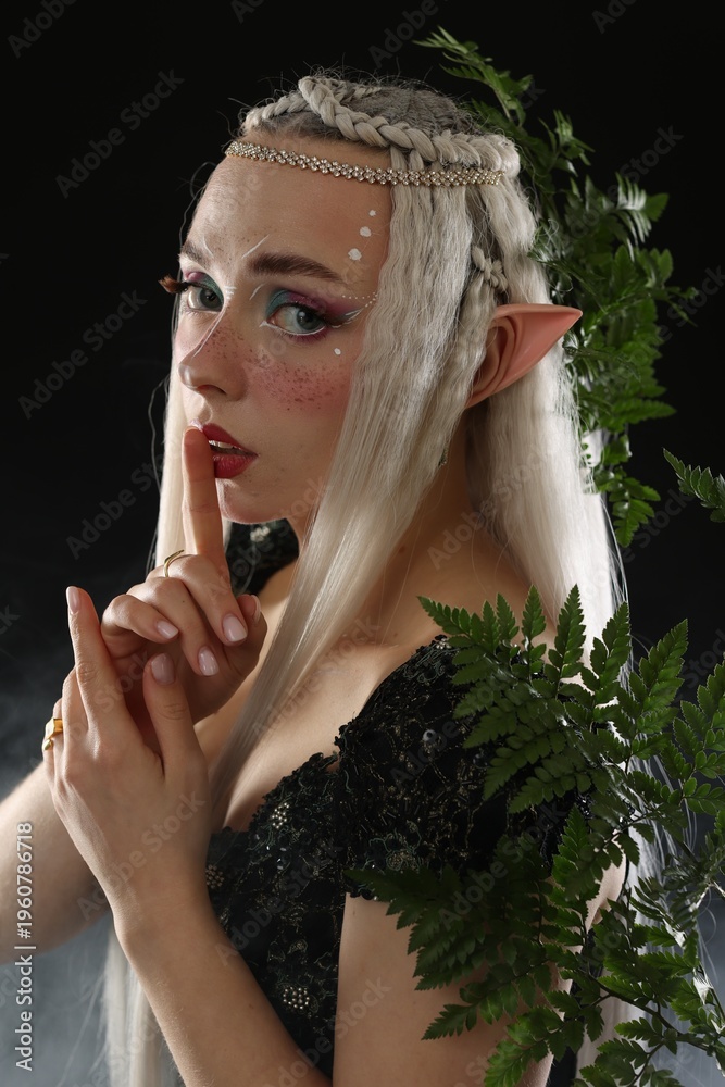 Fototapeta premium Beautiful elf girl with floral decor on black background with smoke