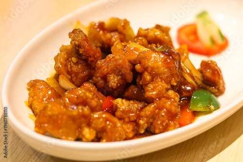 Tableau sur toile Sweet and sour chicken served on a white plate, displayed on a wooden table