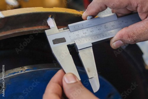 Foto Close up of a mechanic using a steel vernier caliper to measure the internal diameter of a heavy machine component on a yellow industrial engine during a professional maintenance service