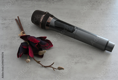Schwarzer Mikrofon und trockene rote Blume auf dem grauen Hintergrund
