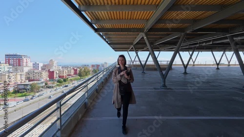 A happy young woman walking across an empty parking lot in Durres, Albania. Urban environment, freedom, lifestyle, casual walk, city scene, outdoor activity, relaxed mood.