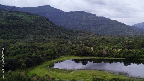 Sideward panning motion flying view of small lake with lush tropical mountainous lanscape and overcast sky in the background