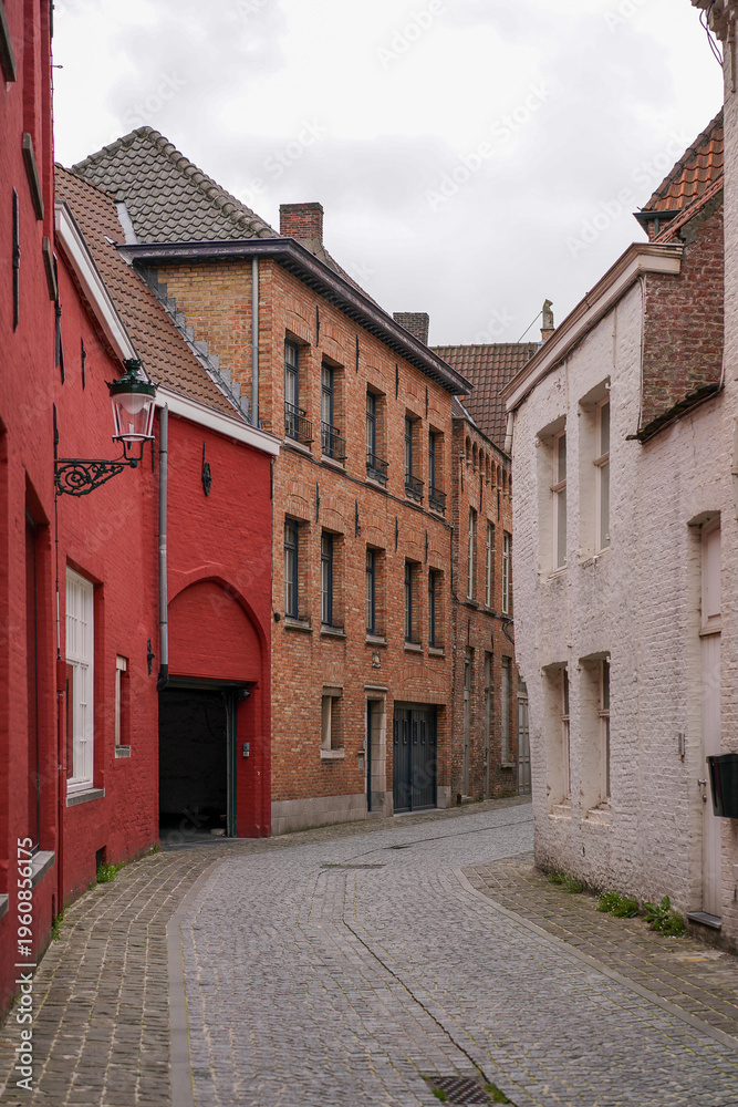 Fototapeta premium Picturesque narrow cobblestone street with red and white brick houses in historic Bruges, Belgium.
