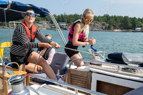 Girl helping mother with cable winch while yachting in sea during vacation trip