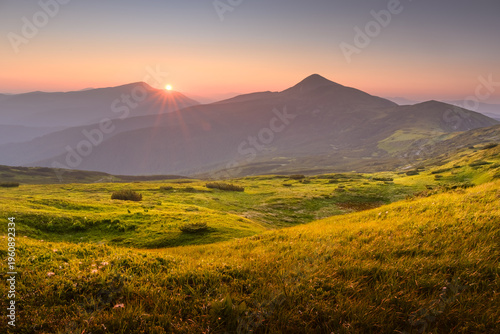 Фотография Incredible sunset with golden sunlight casting a warm glow over lush grassy meadows in the summer mountains