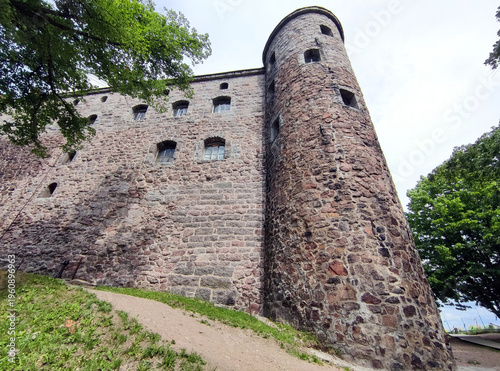 Overview of a medieval stone castle wall at the Vyborg Combined Museum-Reserve, with rugged masonry, small rectangular windows, conical tower, overcast sky. June 6, 2024.