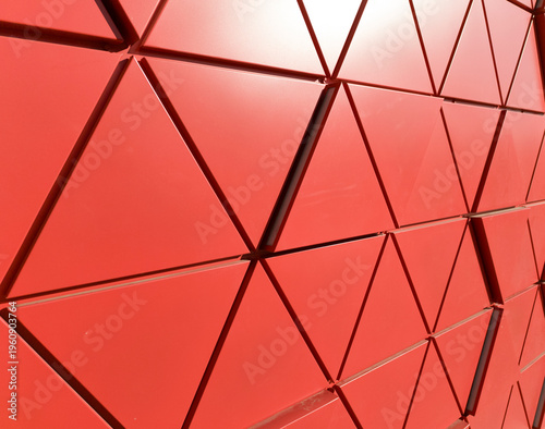 Red geometric facade with triangular panels forming dynamic architectural pattern. Surface structure creates depth and bold composition. Concept of modern design abstract exterior detail..
