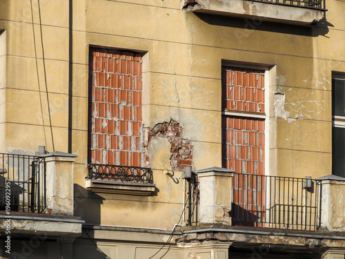 Dilapidated yellow building facade with damaged balconies and bricked up windows