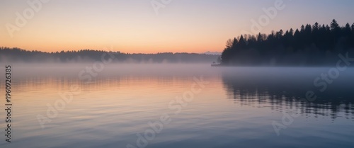 Tranquil Lake at Sunrise with Mist and Reflection Surrounded by Forest Landscape