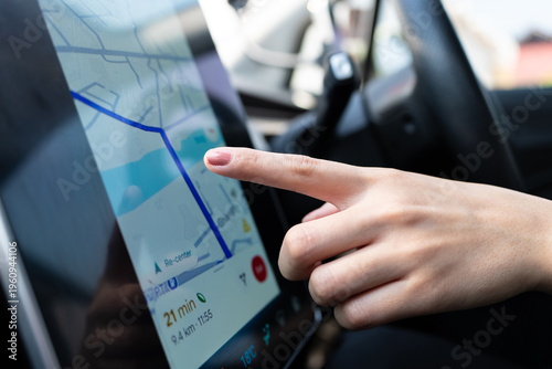 Woman's hand interacts with a modern car's touch screen navigation system for route planning. GPS map, destination, convenient driving technology concept.