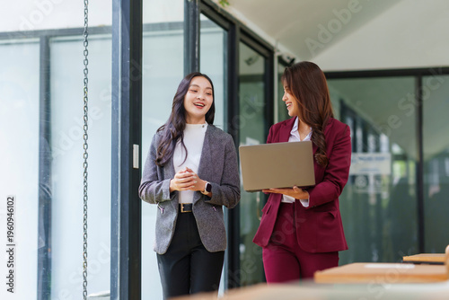 Two Asian businesswomen collegues walking and having a professional discussion, sharing ideas and working together in an office