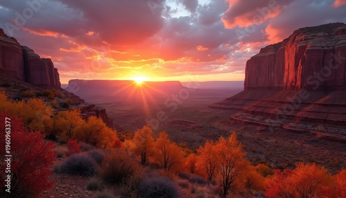 Dramatic sunset glows over desert valley with red rock canyons. Orange and red trees create vibrant autumn foliage contrast. Wide angle view shows vast natural landscape at dusk.
