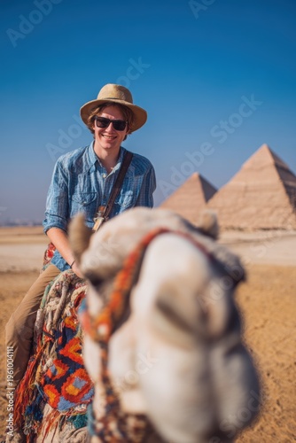 Wallpaper Mural Vacation travel trip journey in holiday season. A man riding a camel in front of the majestic pyramids of Giza. He wears a hat, sunglasses, and a shirt. Torontodigital.ca