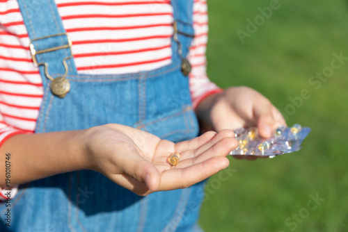 Outdoors, a little girl holds vitamin D drops in her hand
