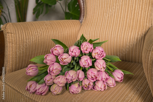 Bouquet of pink tulips on a beige armchair with greenery in the background