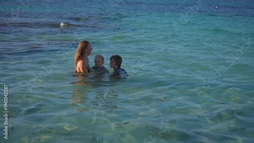 Young mom spending quality time with her two sons on a beautiful tropical beach, enjoying sunshine, laughter, and family bonding moments by the sea.